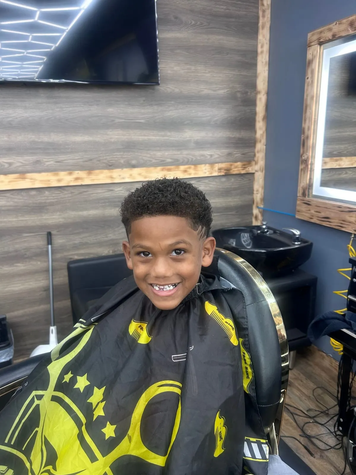 Smiling boy in a gold-and-black cape with a curly top, a faded side and a cut-in line