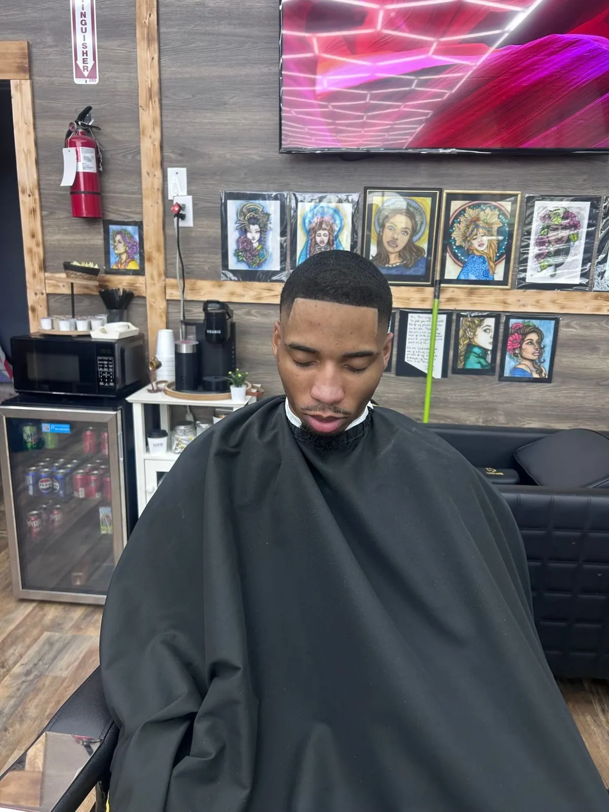 Man with closed eyes in a black cape, a sharp skin fade, a crisp lineup and a trimmed goatee