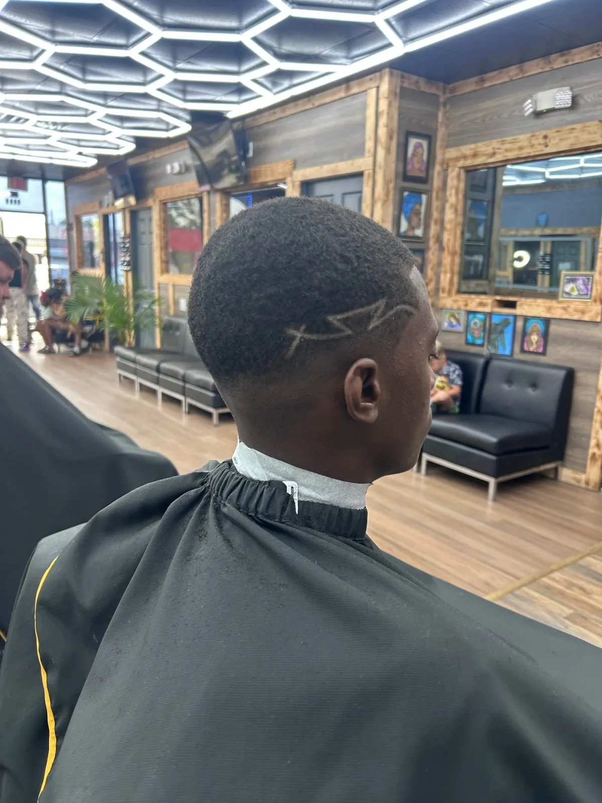 Boy seen from behind in a black cape, with a lightning-bolt design cut into a short fade