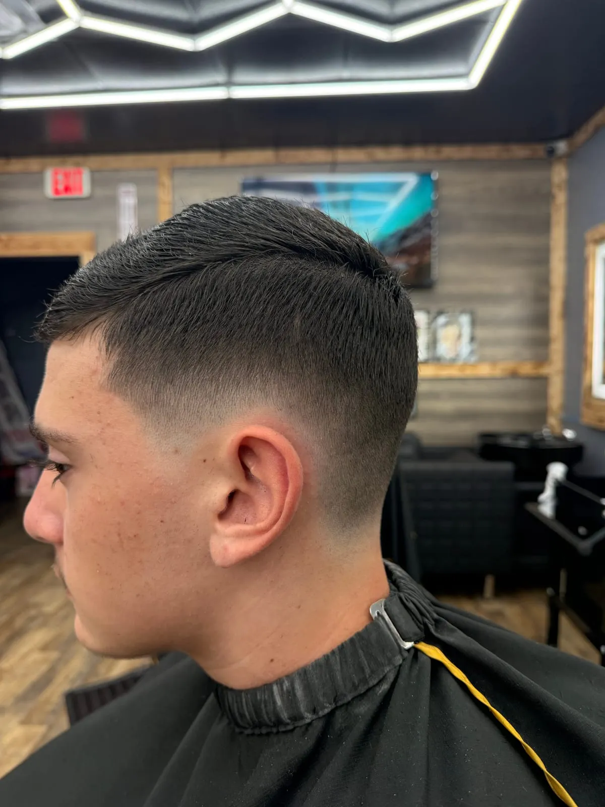 Boy in profile in a black cape with gold trim, with a short dark top and a clean low fade