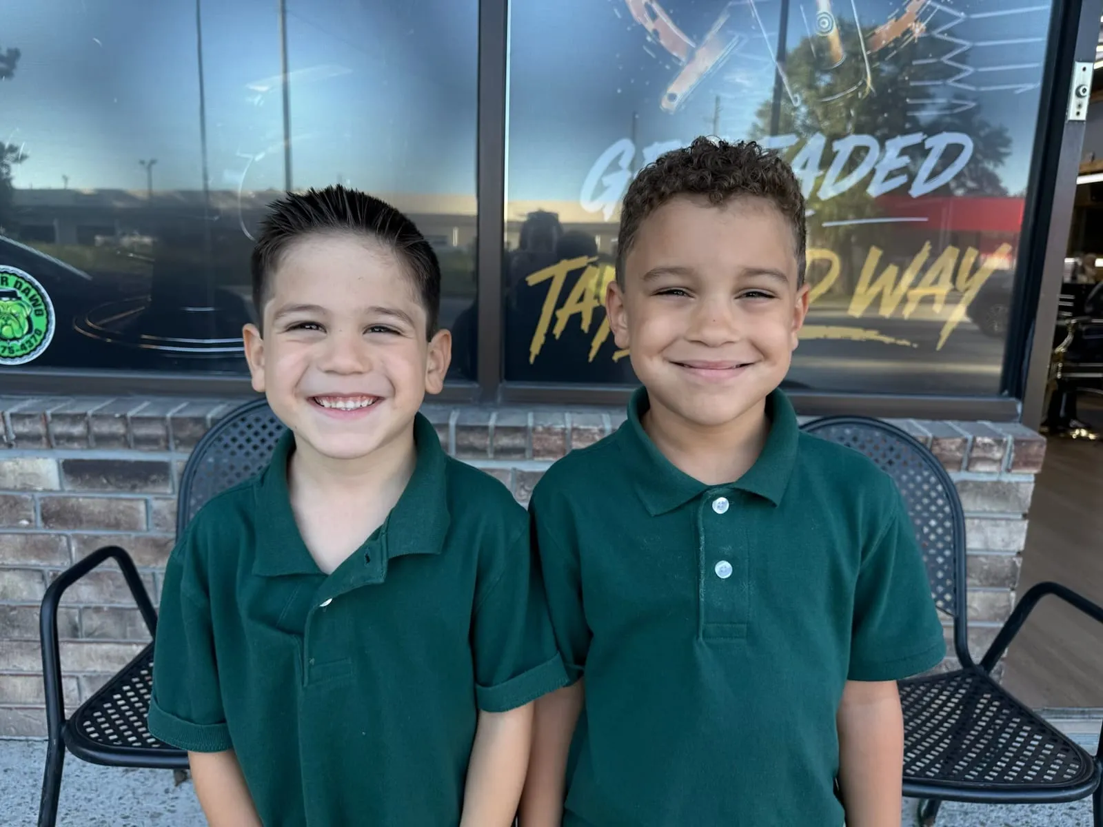 Two smiling boys in matching green polo shirts standing outside the shop with fresh short haircuts