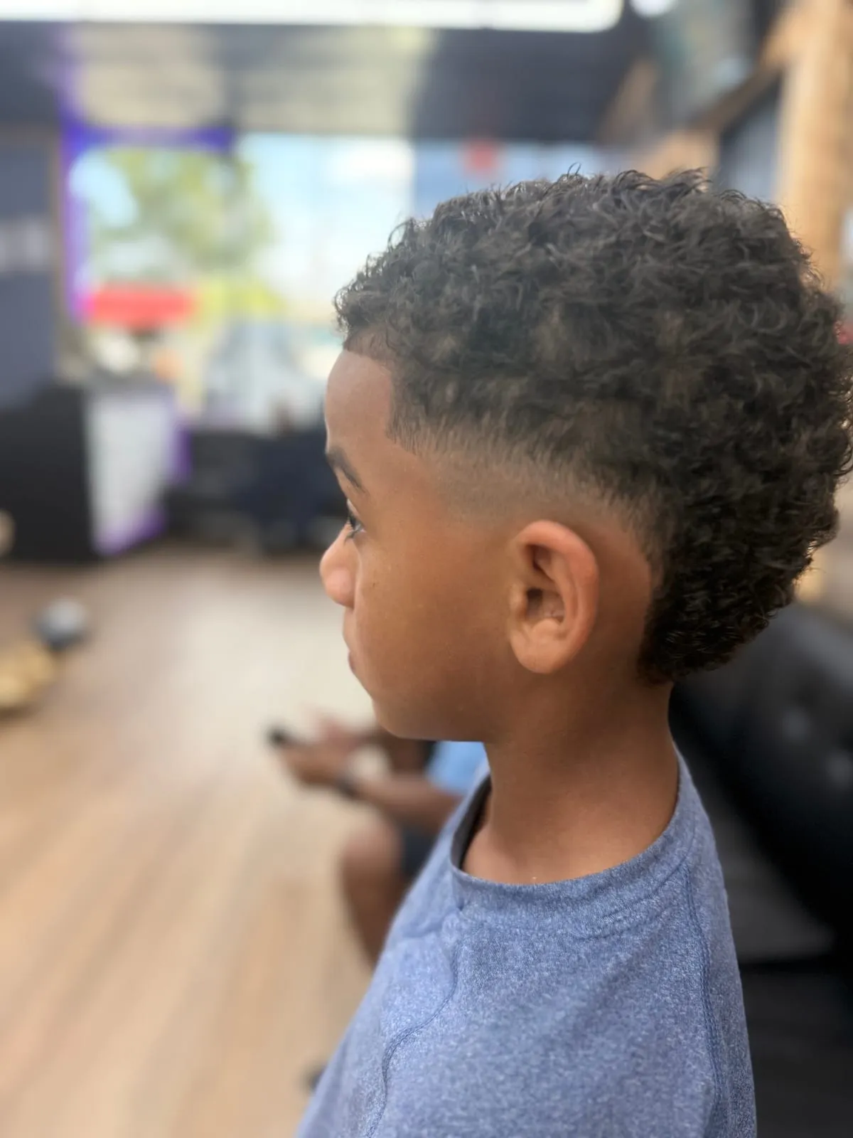 Boy in profile with tight curls on top and a low fade at the sides