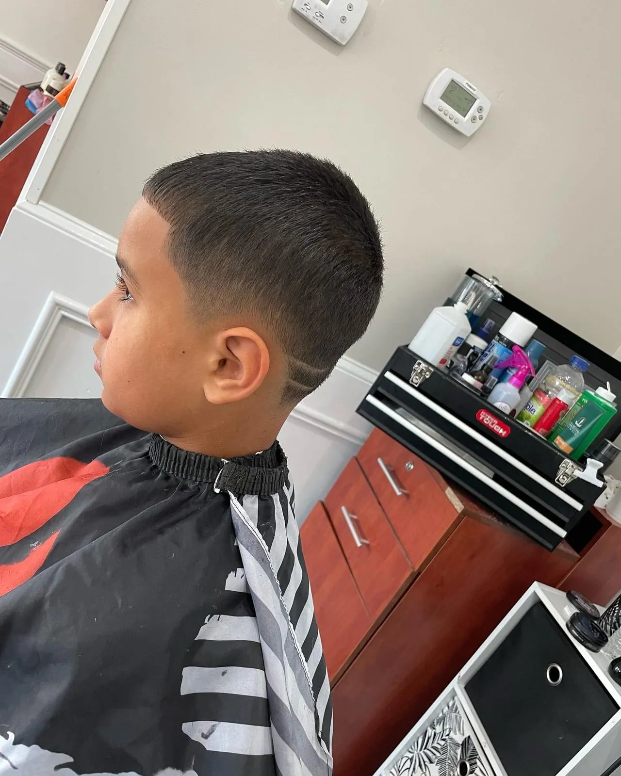 Boy in profile in a black cape with a short top, a clean taper and a cut-in line behind the ear