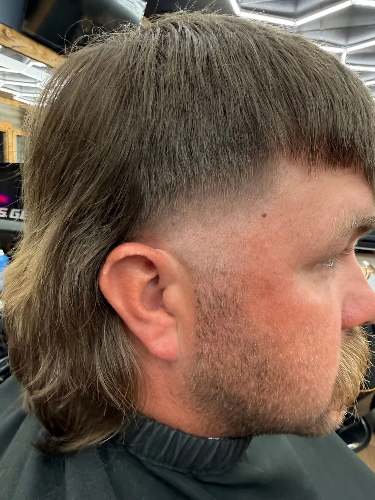 Man in profile with a long mullet and a high skin fade at the temple, with a trimmed beard